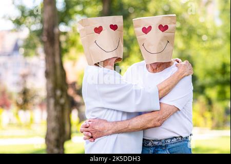 Senior couple in love with paper bags over the head romantic dating - Old people in the age of 60, 70, 80 having fun and spending time together, conce Stock Photo