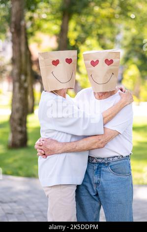 Senior couple in love with paper bags over the head romantic dating - Old people in the age of 60, 70, 80 having fun and spending time together, conce Stock Photo