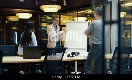 Diverse office workers having meeting, discussing blueprint on flipchart. Presentation of engineering architect startup in modern office of company. Businessman leading conference with managers Stock Photo