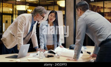 Multi-ethnic team of engineers looking through papers and blueprints, discussing business strategy, working on engineering startup project. Business meeting in office conference room Stock Photo