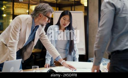 Multi-ethnic team of engineers looking through papers and blueprints, discussing business strategy, working on engineering startup project. Business meeting in office conference room Stock Photo