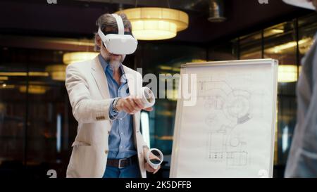 Male engineers using VR headsets and wireless controllers, looking at blueprint in virtual reality, watching data, working in modern office of hi-tech company. Cyberspace digital technology Stock Photo