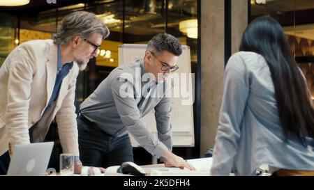 Diverse team of office workers looking through papers, discussing business strategy of company, working on startup project. CEO leading business meeting in conference room. Teamwork and brainstorming Stock Photo