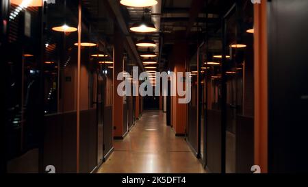 Corridor of modern business center office, e-commerce marketing company, real estate corporation with doors and separate offices, illuminated by lamps Stock Photo