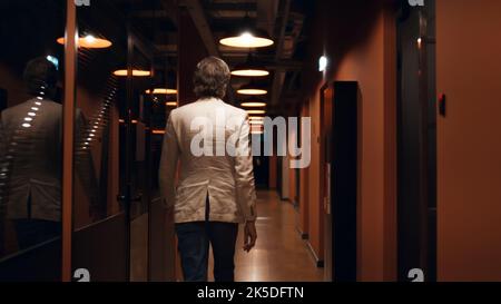 Back view of successful businessman in suit walking in modern corridor. Male office worker going to work. Office hallway of E-commerce marketing company Stock Photo