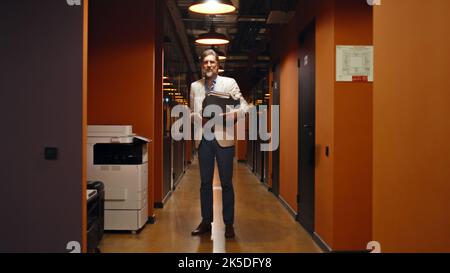 Fired male worker in suit standing in office corridor, holding box with books and personal stuff. Upset man leaving marketing company Stock Photo