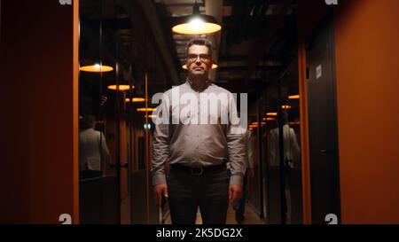 Happy male office worker in suit and glasses standing in office corridor, smiling, looking at camera. Successful mature businessman in hallway of marketing company modern business center Stock Photo