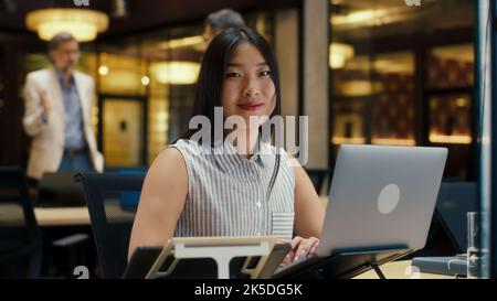 Asian businesswoman looking at the camera while working on business strategy in modern office using laptop and digital tablet. E-commerce company Stock Photo