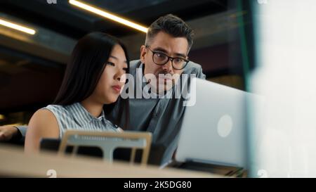 Asian woman consulting with supervisor and discussing business strategy in modern office using laptop and digital tablet. CEO of marketing company with female worker Stock Photo