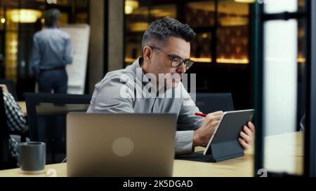 Male office worker, using tablet computer and digital pencil, working in modern office on startup project, business strategy or design of website. Work in IT company Stock Photo
