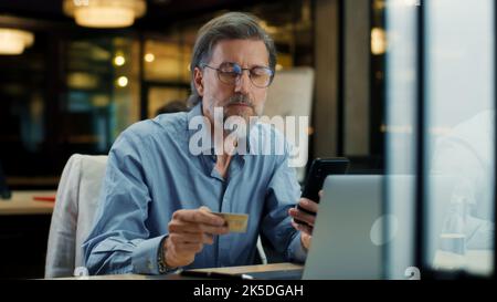 Businessman using phone, transferring money on bank card, paying for service online during work in modern office of IT company Stock Photo