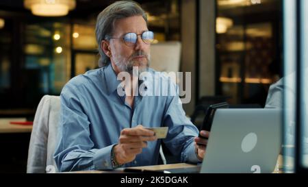Businessman using phone, transferring money on bank card, paying for service online during work in modern office of IT company Stock Photo