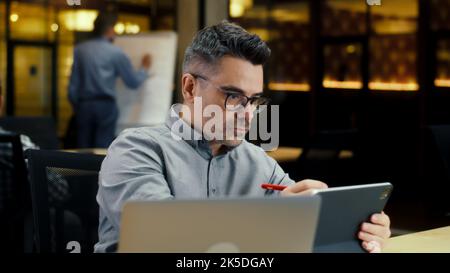 Male office worker, using tablet computer and digital pencil, working in modern office on startup project, business strategy or design of website. Work in IT company Stock Photo