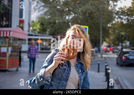 Blonde woman eating traditional Turkish bread bagel on the street. Blonde woman eating traditional Turkish bread bagel on the street.