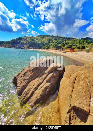 A vertical shot of huge rocks by the sea with people on a sandy beach in the background Stock Photo