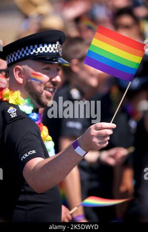 Brighton & Hove Pride Festival, Brighton & Hove, East Sussex, England. British policeman in uniform with rainbow flag painted on face and being waved in hand Stock Photo