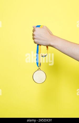 Hand holding a medal with blue and yellow ribbon Stock Photo - Alamy