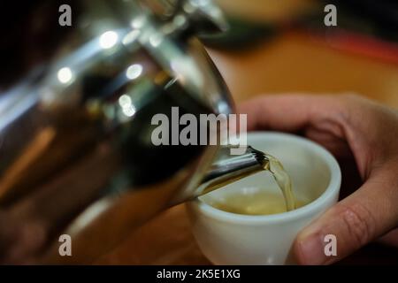 Close up hot tea pouring into a white cup. Blurry lights on black background. Pouring tea into cup from teapot. Nobody, blurred, selective focus Stock Photo