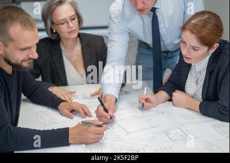 Four colleagues are discussing blueprints in a conference room in an office. Brainstorming of engineers and architects. Stock Photo