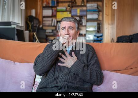 Sick man sitting at home and with a coughing fit from respiratory diseases. Stock Photo