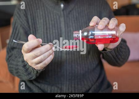 Sick man pouring syrup into a spoon to take it and alleviate the symptoms of the disease. Stock Photo