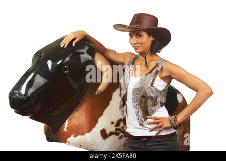 Shes a professional at the mechanical bull. Studio shot of a beautiful young cowgirl standing next to a mechanical bull against a white background. Stock Photo