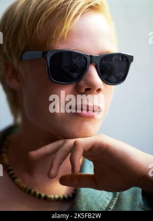 Contemplating cool. Attractive young guy wearing hipster shades with his hand on his chin. Stock Photo