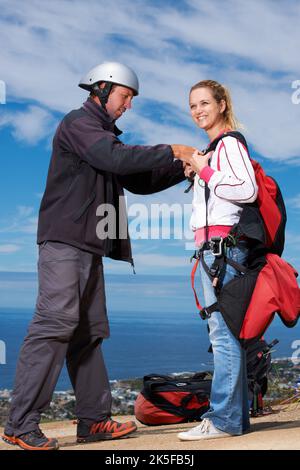 Doing a quick safety check. A paragliders smiling as her instructor helps her tighten her straps. Stock Photo