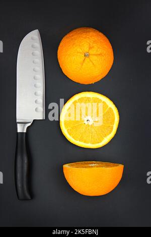 Sharp stainless steel knife and fresh orange on dark background Stock Photo