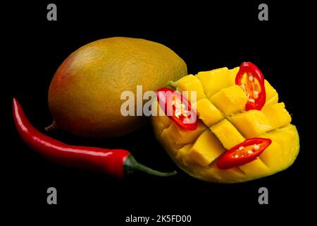 Whole mango, whole chili pepper, sliced hot pepper and cutted half of mango isolated on black background. Ingredients for Spicy mango chutney. Soft fo Stock Photo