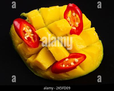Close-up of diced half of mango and sliced red hot pepper on solid black background. Ingredients for salad. Stock Photo
