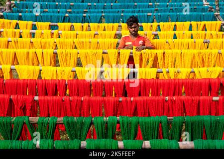 Workers hang thousands of freshly dyed colorful threads on a wooden structure as they are being dried in the sunshine. Stock Photo