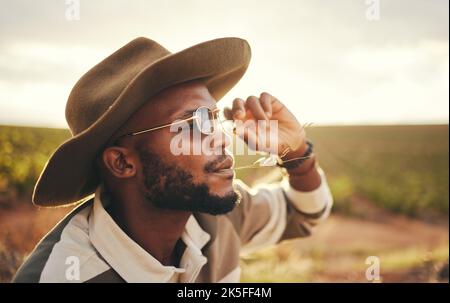 Sustainability, farm and agriculture with a black man or cowboy farmer chewing straw in a grass field or meadow. Sustainable, farming and sustainable Stock Photo