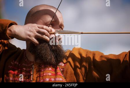 Medieval archery tournament. Man shoots an arrow in the medieval castle yard. Man in medieval dress with a wooden bow in her hands. historical Stock Photo