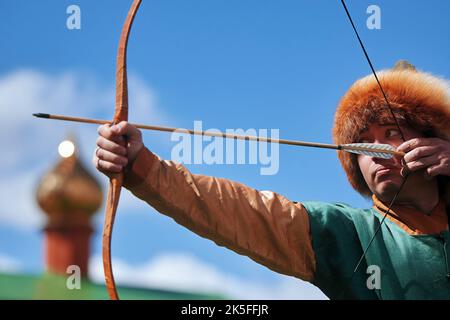 Medieval archery tournament. Man shoots an arrow in the medieval castle yard. Man in medieval dress with a wooden bow in her hands. historical Stock Photo