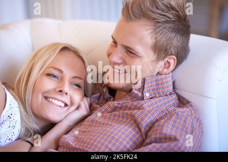 Together and in love. A happy couple lying on the couch together and laughing. Stock Photo