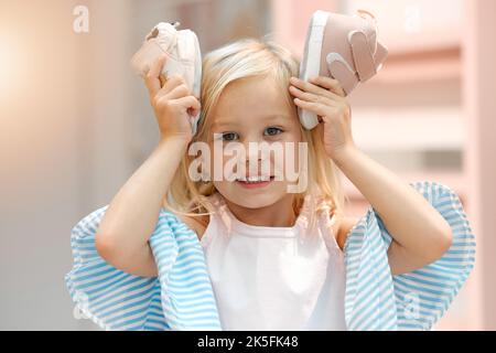 Children, fashion and clothes with shoes in girl hands against her head while shopping in a retail store. Kids, cute and choice with a female child Stock Photo