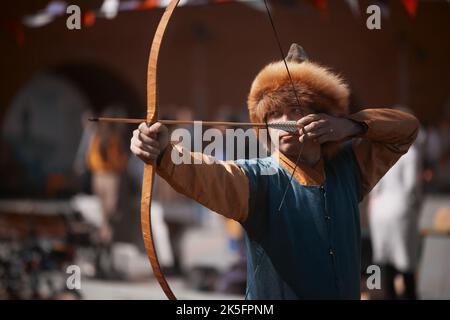 Medieval archery tournament. Man shoots an arrow in the medieval castle yard. Man in medieval dress with a wooden bow in her hands. historical Stock Photo