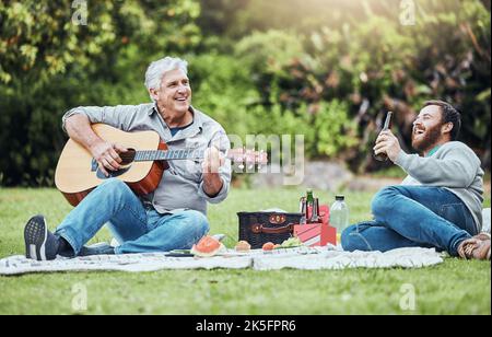 Guitar, father and son on park picnic with beer and music during holiday in Australia in summer. Senior dad and man laughing at comic sound on Stock Photo