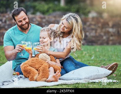 Children, family and picnic with a girl, mother and father sitting outdoor on a grass field in a park with a drink or glass of juice. Kids, summer and Stock Photo