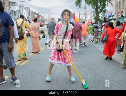 A Hindu girl sweeping a path where deities will pass. On Liberty Avenue during the Ratha Yatra parade in Ozone Park, Queens, New York. Stock Photo