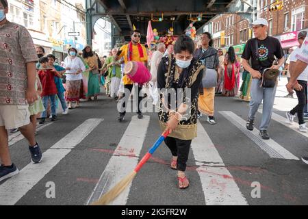 A Hindu woman sweeping a path where deities will pass. Under the elevated subway during the Ratha Yatra parade in Ozone Park, Queens, New York. Stock Photo