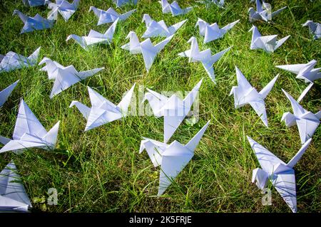 Japanese folded Origami cranes on fresh grass. Hundreds handmade paper birds on green field with copy space. 1000 thousand crane tsuru sculpture topic. Symbol of peace, faith, health, wishes and hope  Stock Photo
