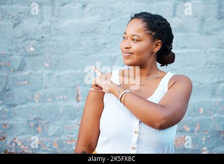 Black woman pointing finger to show advertising, promo or commercial mockup, marketing space on blue wall outdoor gen z, youth lifestyle. African girl Stock Photo
