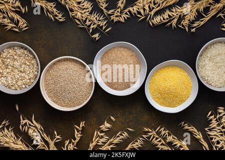 Various grain cereals in bowls, top view on a brown background with bowls of cereals and ears of oats Stock Photo