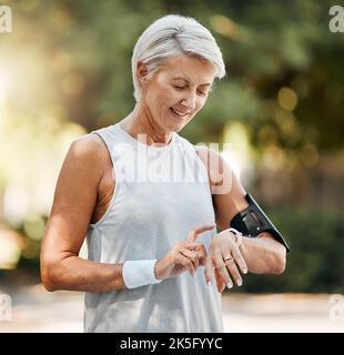Senior woman, fitness and watch of running time in health and wellness for cardio exercise in nature. Active elderly female runner checking smartwatch Stock Photo