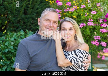 Happy middle aged couple posing arm in arm in a loving family portrait outdoors in a summer garden Stock Photo