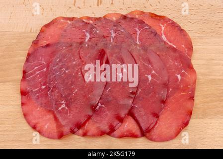Bresaola slices, italian dried beef salami from Valtellina on wooden background Stock Photo