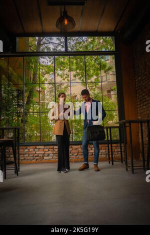 A young business couple is leaving the coffee bar after working online, on a cloudy day Stock Photo