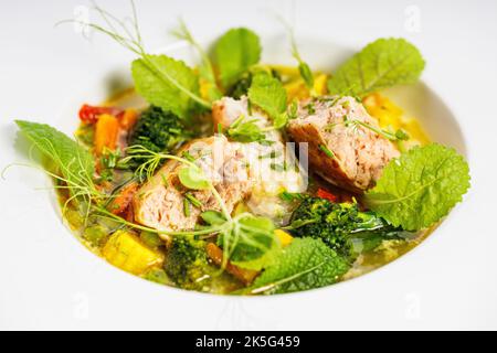 Close-up salmon cutlet with fish broth and vegetables. Appetizing fish meatballs with vegetable pesto soup. Served on a white plate. Selective focus. Stock Photo